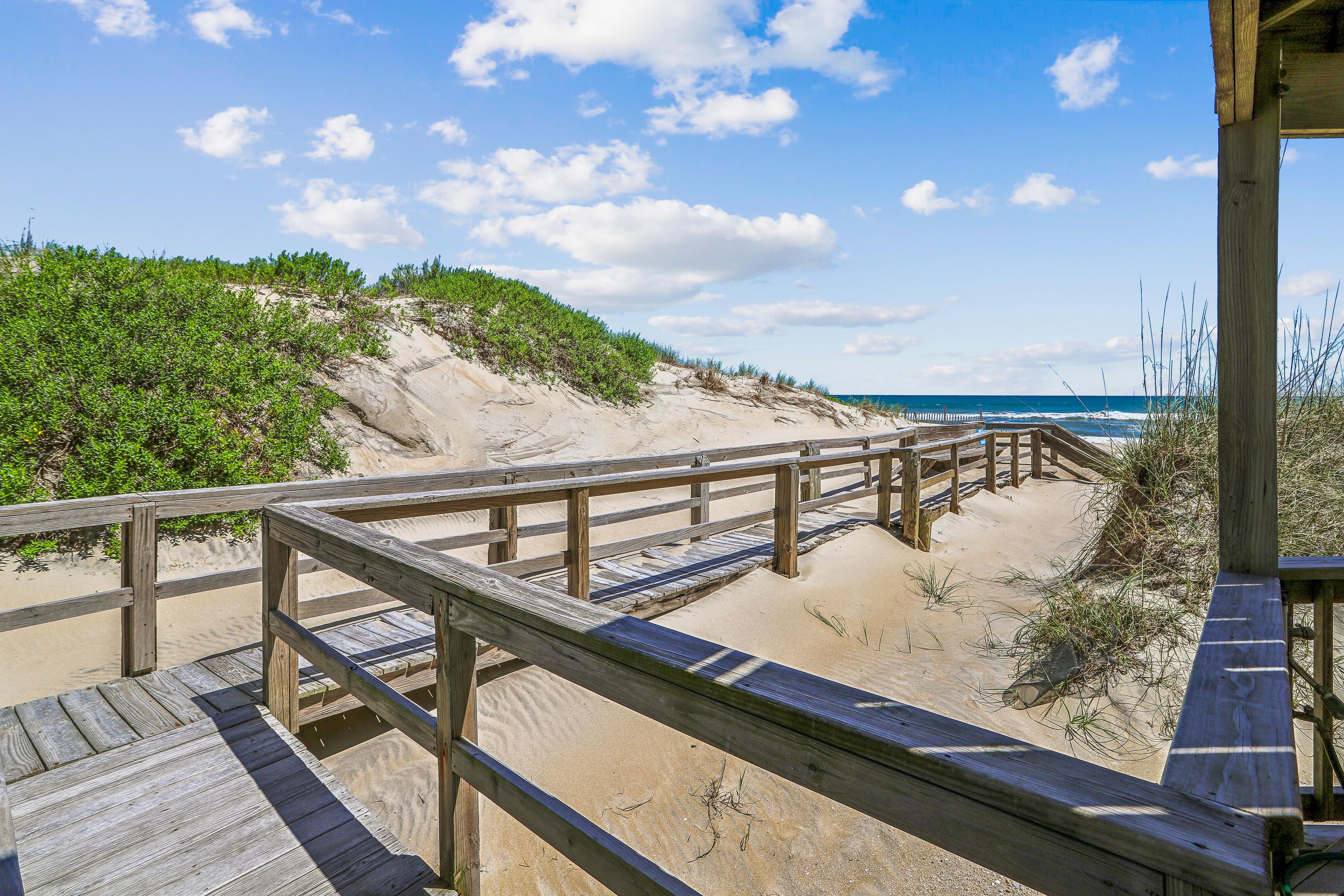 A wooden boardwalk leading to a sandy beach with a clear view of the ocean.