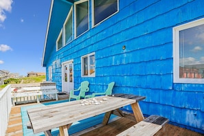 A blue wooden house with a deck, a table, and two chairs.