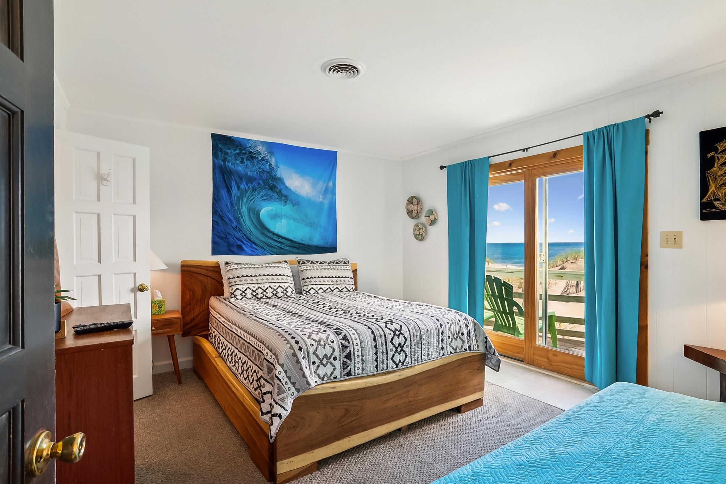 A bedroom with a bed, a view of the beach, a door, and a window with curtains.