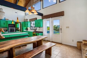 A kitchen with green cabinets, a wooden bench, and a view of the outdoors through a door.
