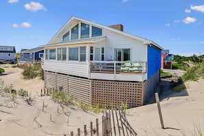 A beachfront house with a balcony, large windows, and a wooden fence.