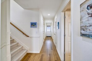 Un corridoio con una scala in legno, pareti bianche e pavimento in legno.