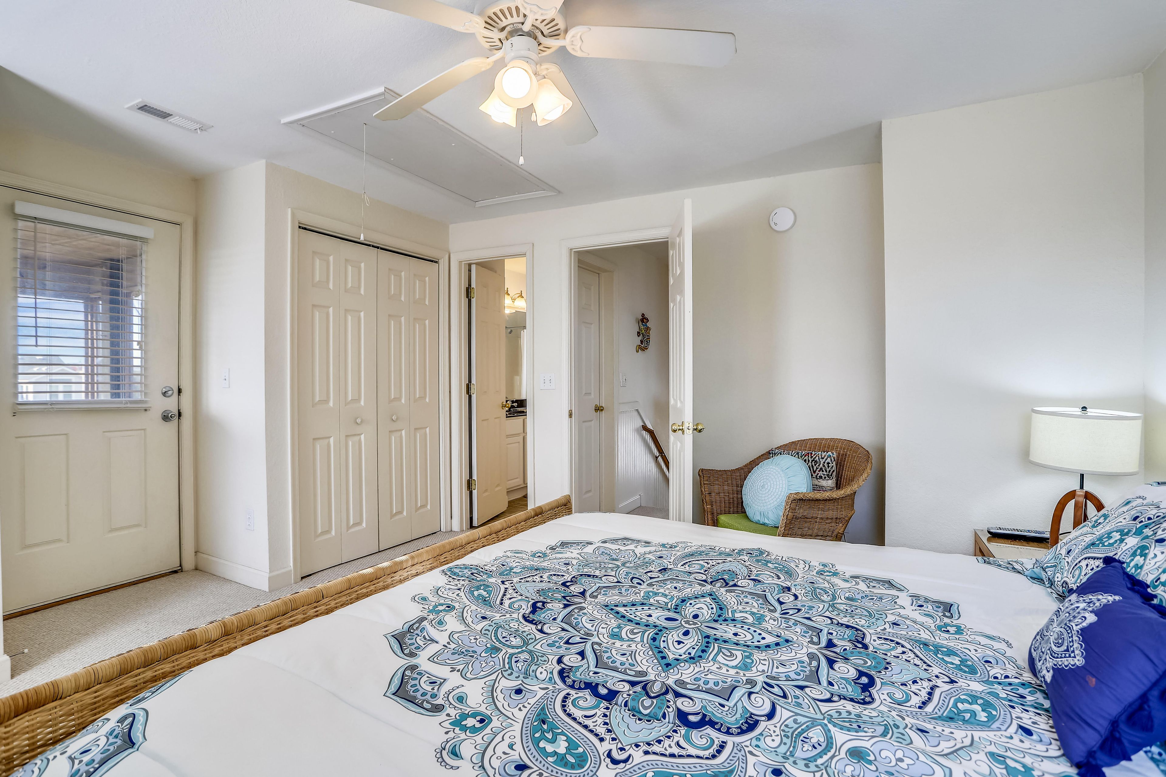 A bedroom with a bed, a ceiling fan, a door, and a chair.