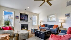 A living room with a fireplace, a ceiling fan, and a blue sofa with orange cushions. - Miller Cottage -- Semi OF Home in Kitty Hawk with Hot Tub (Kitty Hawk)