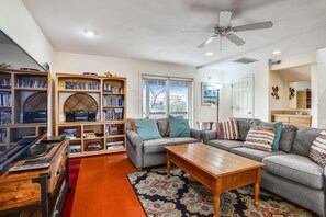 A living room with a sofa, a coffee table, a bookshelf, and a ceiling fan. - Miller Cottage -- Semi OF Home in Kitty Hawk with Hot Tub (Kitty Hawk)