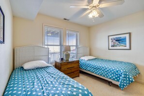 A bedroom with two beds, a ceiling fan, a nightstand, and a window with blinds.