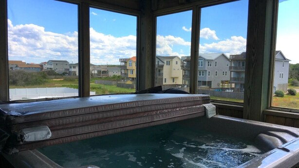 A hot tub with a view of residential buildings through large windows. - Miller Cottage -- Semi OF Home in Kitty Hawk with Hot Tub (Kitty Hawk)