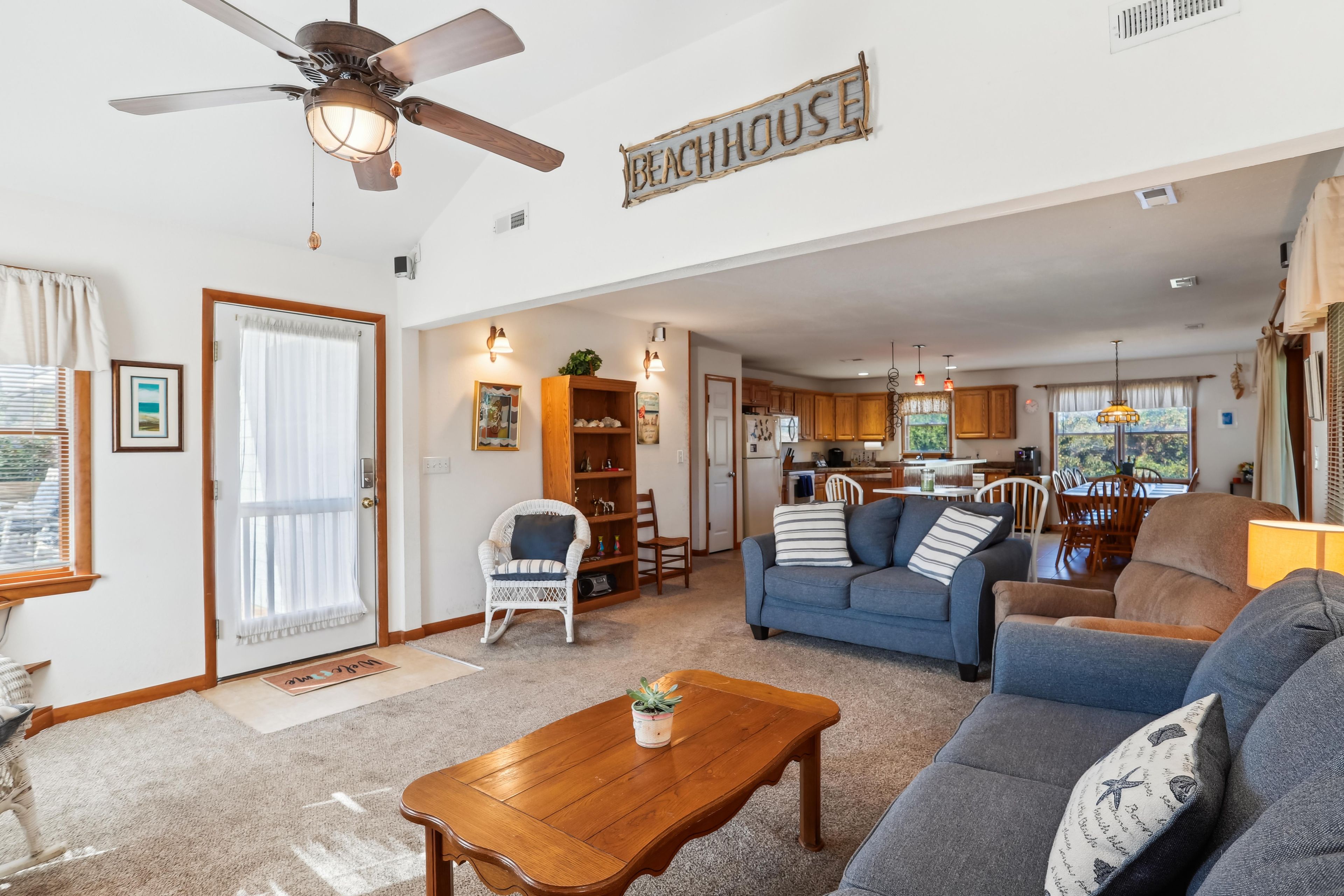 A spacious living room with a ceiling fan, a dining area, and a kitchen with wooden cabinets.