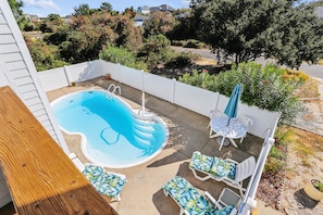 Un patio trasero con piscina, sillones de descanso y una mesa con sombrilla.
