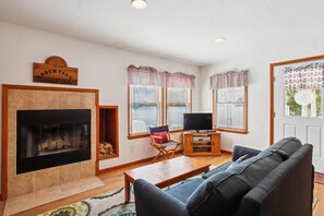 A living room with a fireplace, a television on a wooden stand, a sofa, and a window with striped curtains.