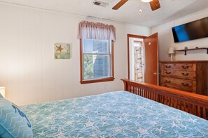 A bedroom with a bed, a dresser, a television, and a window with blinds.