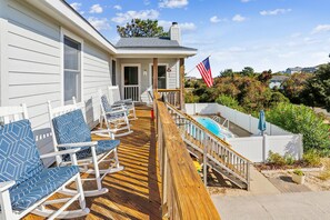 A wooden deck with rocking chairs, a pool, and an American flag.