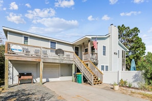 A two-story house with a front porch, a garage, and a small outdoor basketball hoop. - Tax D'Ducktion-- 6BR Oceanside home in Downtown Duck with Pool (Duck)