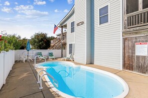 A residential swimming pool with a wooden deck, lounge chairs, and a flag.