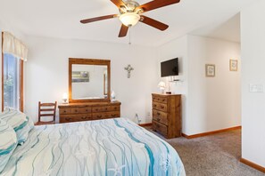 A bedroom with a bed, a wooden dresser, a vanity with a mirror, a ceiling fan, and a television on the wall. - Tax D'Ducktion-- 6BR Oceanside home in Downtown Duck with Pool (Duck)