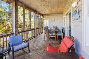 A covered porch with wooden flooring, a dining table with chairs, and a bench. - Tax D'Ducktion-- 6BR Oceanside home in Downtown Duck with Pool (Duck)