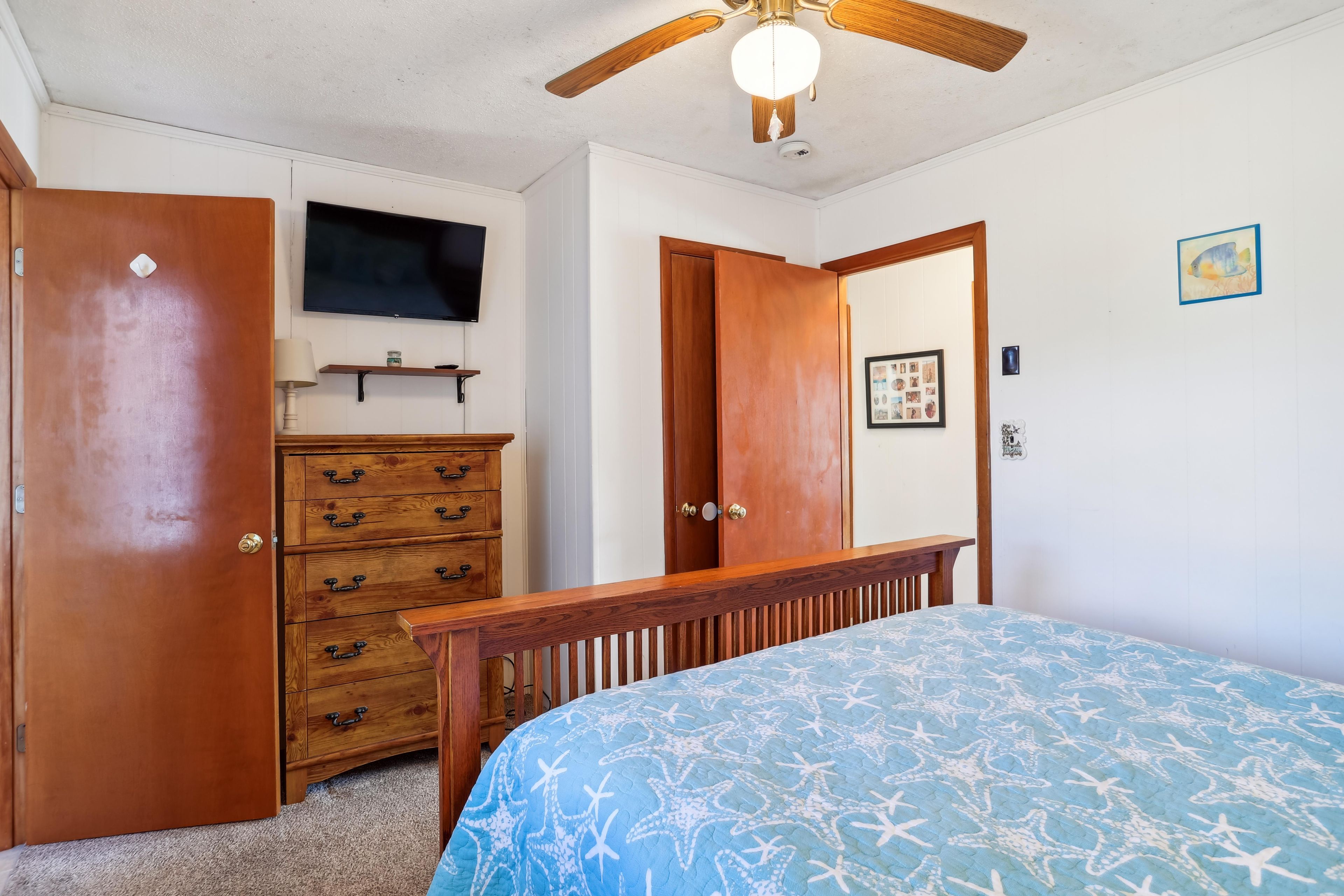A bedroom with a bed, a dresser, a television, and a ceiling fan.