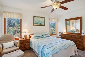Ein Schlafzimmer mit Bett, Sessel, Nachttisch, Kommode, Deckenventilator und einem Bild an der Wand.