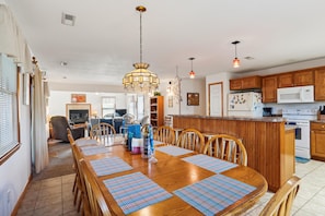 A spacious kitchen with wooden cabinets, a central island, and a dining area with a large wooden table and chairs. - Tax D'Ducktion-- 6BR Oceanside home in Downtown Duck with Pool (Duck)