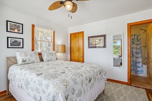 Quarto com cama, janela com persianas, porta, ventilador de teto e quadros na parede.