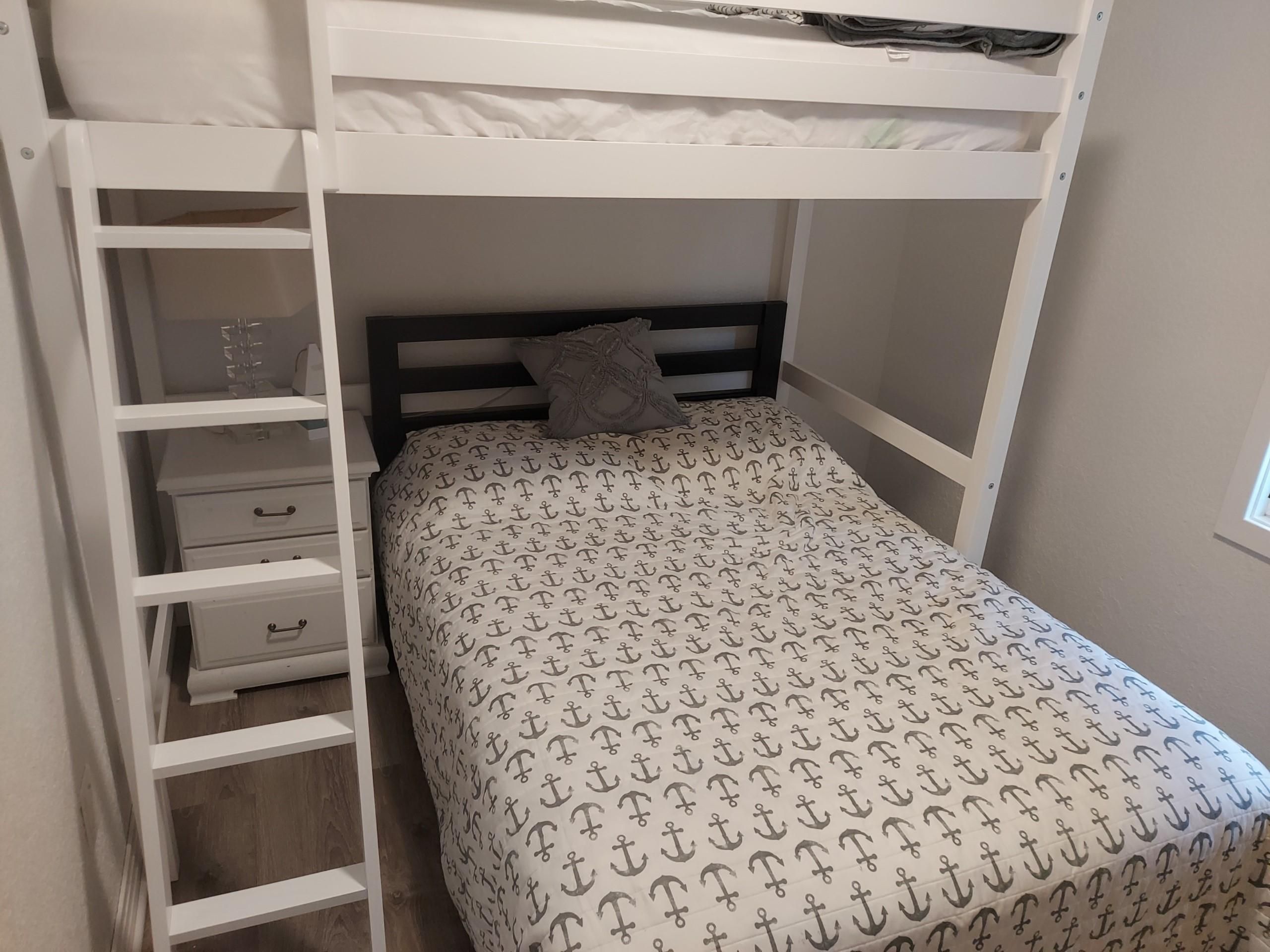 A bunk bed with a patterned bedspread, a pillow, and a storage unit with drawers.