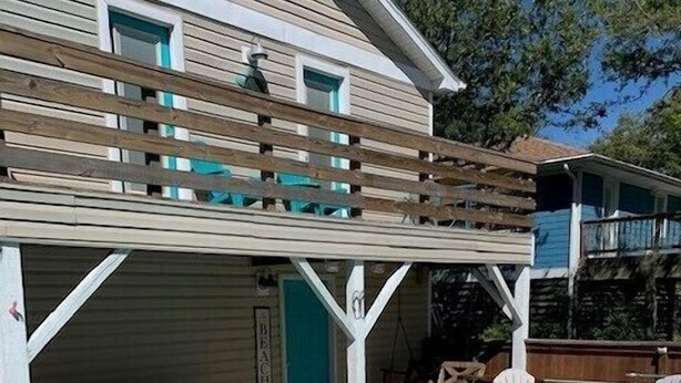 A swimming pool with a wooden deck and chairs, a covered patio area, and a building with a 'Beach' sign. - Flamingo -- Pet Friendly Home with Private Pool and Gameroom (Nags Head)