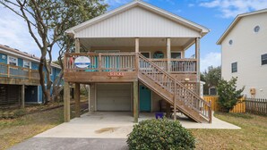 A two-story residential building with a front porch, a staircase leading to the upper level, and a garage door. - Flamingo -- Pet Friendly Home with Private Pool and Gameroom (Nags Head)