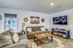 A living room with a sofa, a coffee table, a TV, and decorative items on the wall. - Flamingo -- Pet Friendly Home with Private Pool and Gameroom (Nags Head)