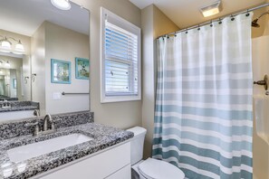 A bathroom with a granite countertop sink, a toilet, a shower curtain, and a window with blinds. - Paws in the Sand -- Gorgeous Pet Friendly Home with Pool (Kitty Hawk)