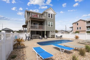 A two-story house with a backyard pool, outdoor furniture, and a fenced patio area. - Paws in the Sand -- Gorgeous Pet Friendly Home with Pool (Kitty Hawk)