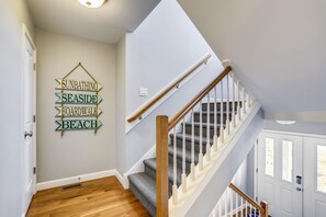A staircase with wooden handrails and carpeted steps leading to a landing with a wall-mounted sign. - Paws in the Sand -- Gorgeous Pet Friendly Home with Pool (Kitty Hawk)