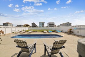 A swimming pool with lounge chairs, a white fence, and houses in the background. - Paws in the Sand -- Gorgeous Pet Friendly Home with Pool (Kitty Hawk)
