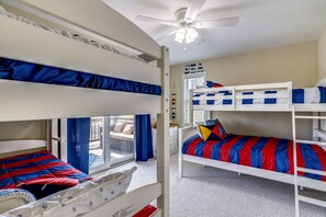 A bunk bed room with a ceiling fan, a window with blue curtains, and a view of the outside. - Paws in the Sand -- Gorgeous Pet Friendly Home with Pool (Kitty Hawk)