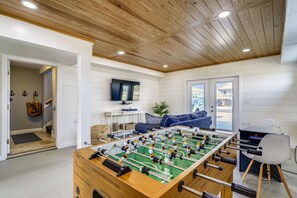 A room with a wooden ceiling, a foosball table, a TV, and a sofa.