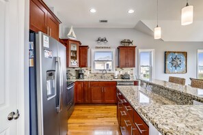 A modern kitchen with wooden cabinets, stainless steel appliances, and a granite countertop. - Paws in the Sand -- Gorgeous Pet Friendly Home with Pool (Kitty Hawk)