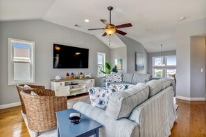 A spacious living room with a large flat-screen TV, a ceiling fan, and a comfortable sectional sofa. - Paws in the Sand -- Gorgeous Pet Friendly Home with Pool (Kitty Hawk)
