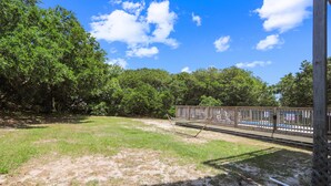 A fenced outdoor area with a hammock, trees, and a clear sky. - Ola Corolla -- Pet Friendly Oceanside home with Pool, Hot Tub (Corolla)