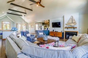 A spacious living room with a large sofa set, a dining area with a kitchen in the background, and a fireplace. - Ola Corolla -- Pet Friendly Oceanside home with Pool, Hot Tub (Corolla)