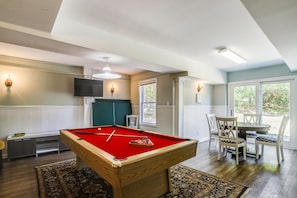 A pool table in a room with a television, chairs, and a view of greenery outside. - Ola Corolla -- Pet Friendly Oceanside home with Pool, Hot Tub (Corolla)