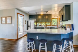 A kitchen with a central island, bar stools, and a refrigerator. - Ola Corolla -- Pet Friendly Oceanside home with Pool, Hot Tub (Corolla)