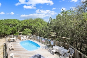 Um deck de madeira com piscina, cadeiras de descanso e um cercado de madeira.