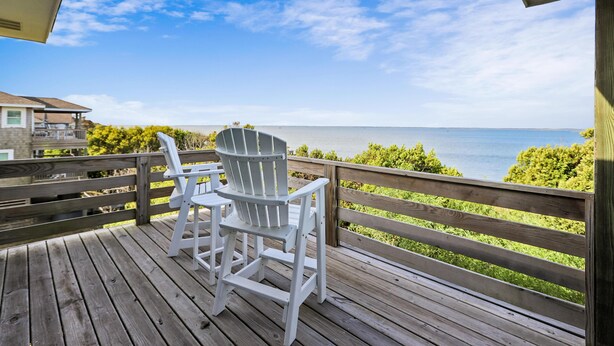A wooden deck with two white Adirondack chairs overlooking a body of water.