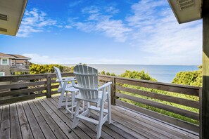 En træterrasse med to hvide Adirondack-stole med udsigt over vandet.