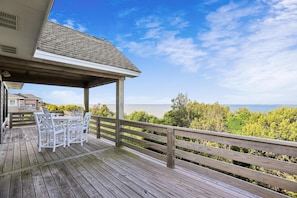 A wooden deck with outdoor furniture, a railing, and a view of the ocean.
