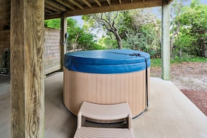 A hot tub under a wooden pergola with a wooden chair in front.