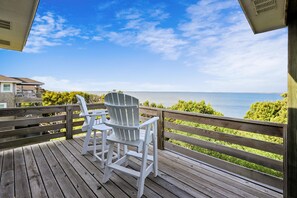 Une terrasse en bois avec deux chaises Adirondack blanches, toutes deux orientées vers un plan d’eau.