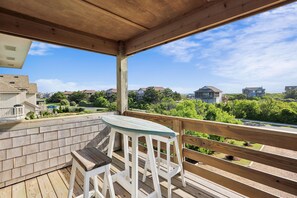 Een houten terras met een tafel en stoelen, met uitzicht op een woonwijk met huizen en groen.
