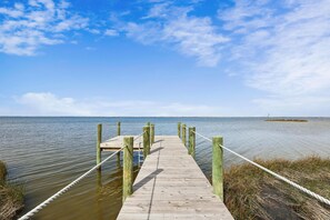 Une jetée en bois s’étendant sur une étendue d’eau calme, sous un ciel dégagé.