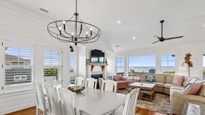A spacious living area with a dining table, white chairs, a sofa, and a ceiling fan.