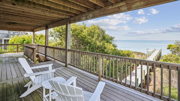 Un pontile in legno con poltrone Adirondack bianche e vista sull'oceano.